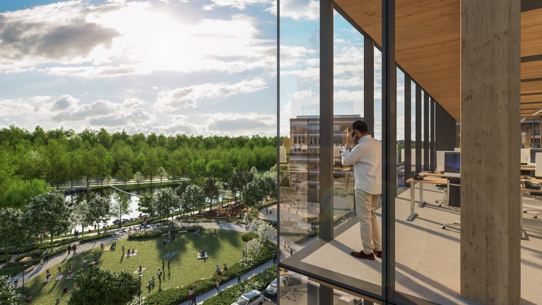 Image of man looking out a large glass window at an expansive green park.